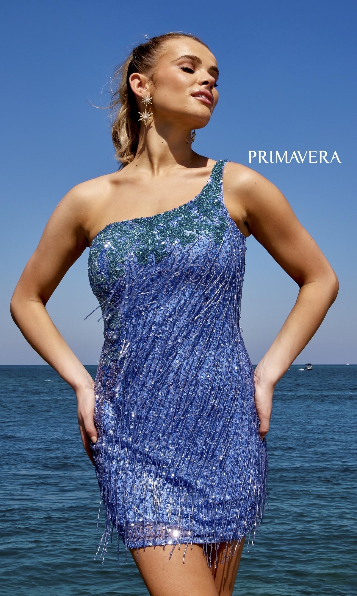 A woman in the Two-Tone Short Fringe Sequin Party Dress 4035 stands by the ocean under a clear sky.